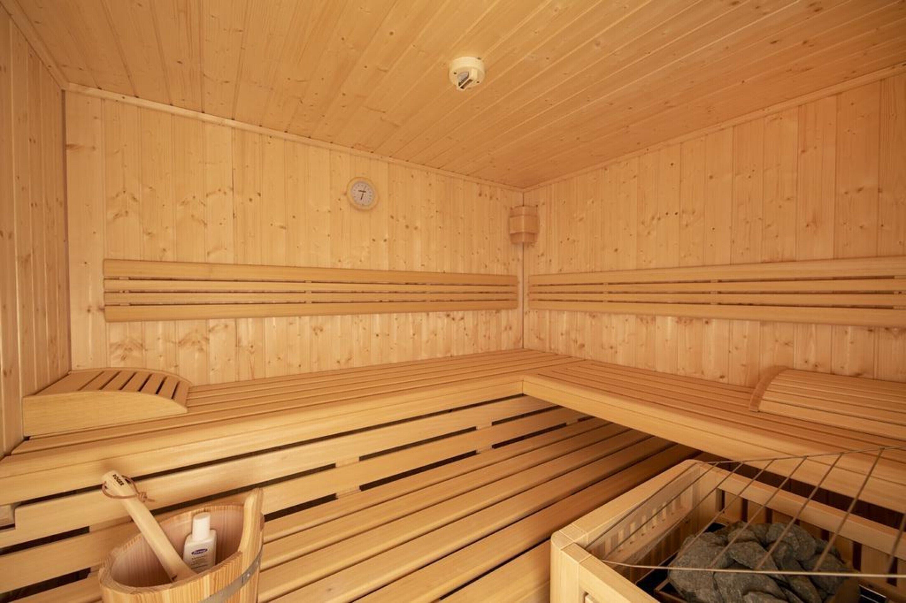 Eine Holzsauna mit Bänken und einem Eimer, der eine Flasche und einen Besen enthält.