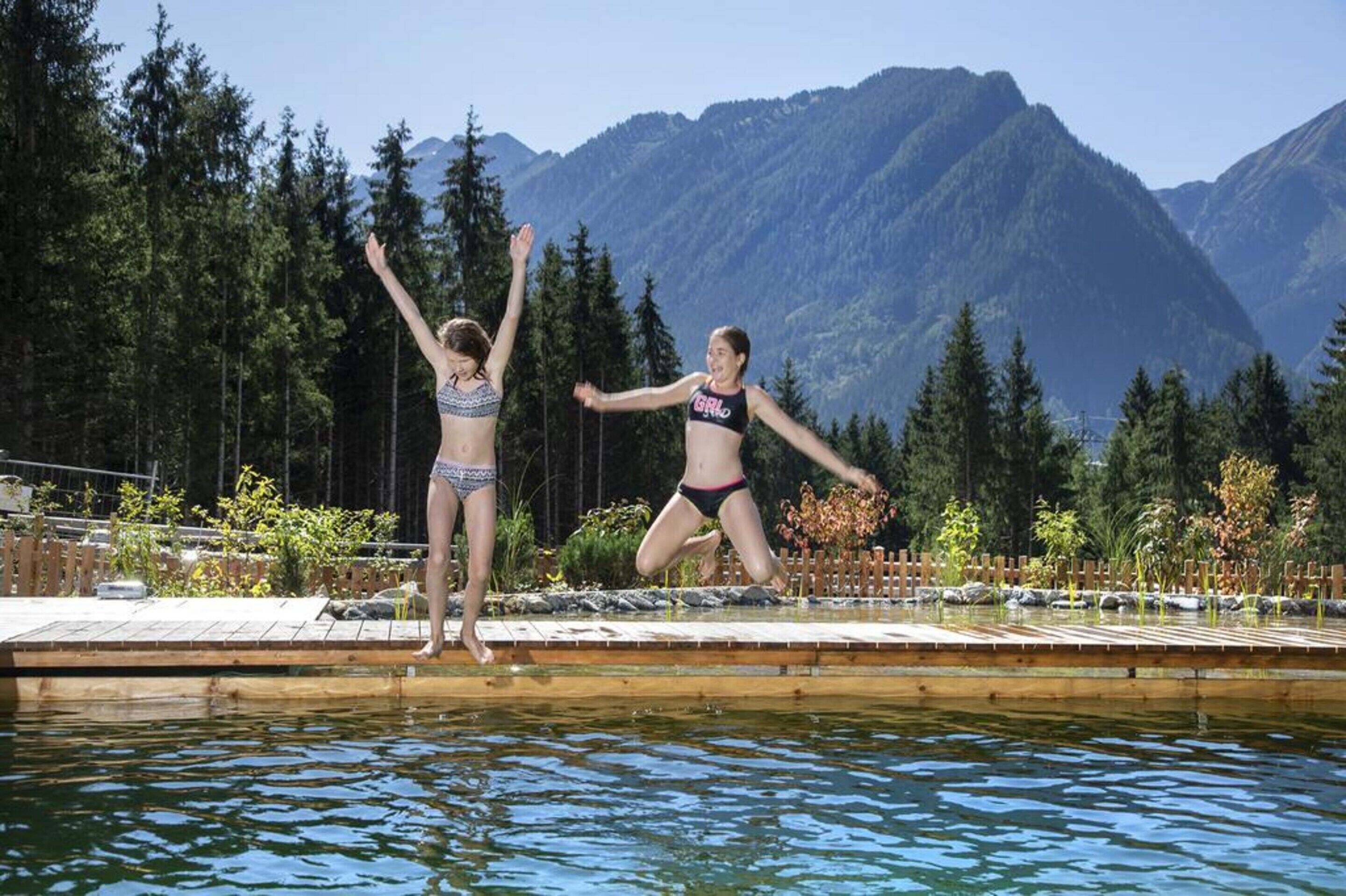 Två personer som hoppar i ett pool med ett bergigt landskap i bakgrunden.