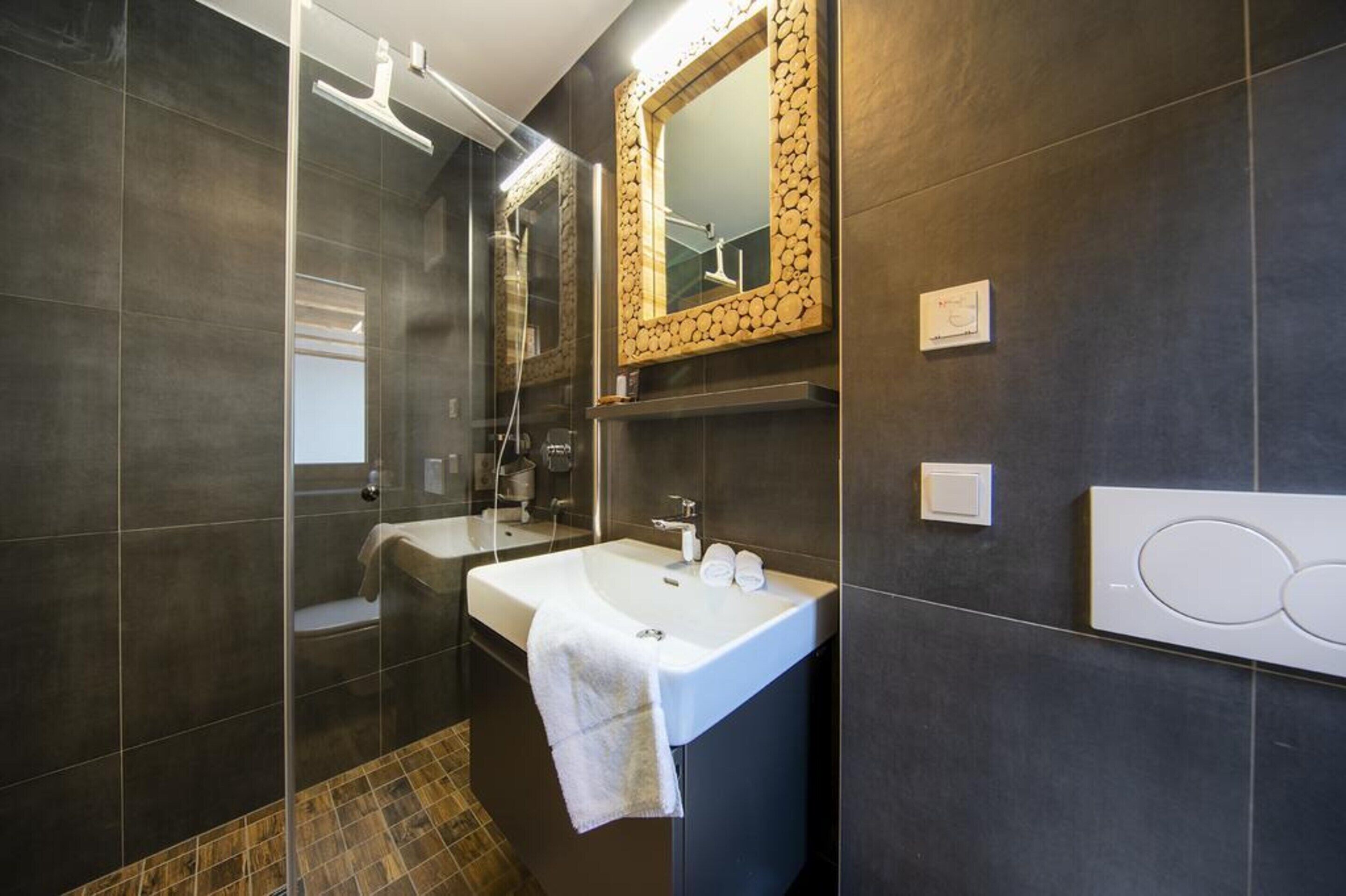 Un baño moderno con ducha de vidrio, lavamanos blanco y espejo con marco de madera.