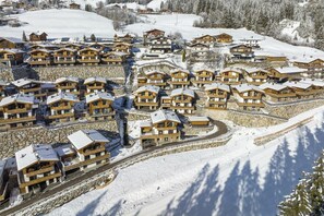 A snow-covered resort with wooden buildings arranged in a semi-circular layout, connected by a stone pathway. - Chalet in Neukirchen by the Ski Area (Neukirchen am Grossvenediger)