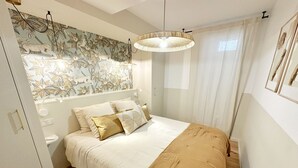 Ein Schlafzimmer mit Bett, Nachttisch, Wandlampe und einem Fenster mit Vorhängen.