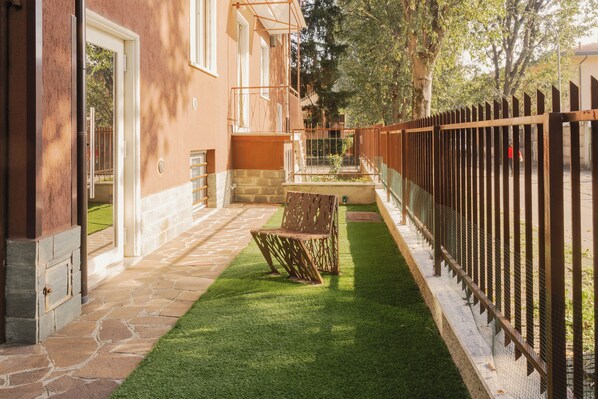 A courtyard with a stone pathway, a wooden bench, and a metal fence. - Residence I Tigli (Cinisello Balsamo)