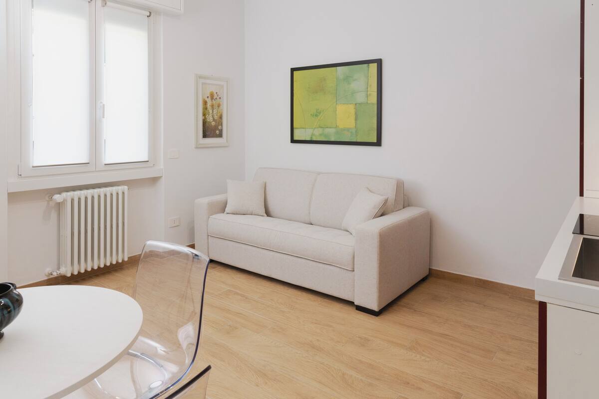 Una sala de estar moderna con un sofá color beige, una mesa de vidrio y un radiador.