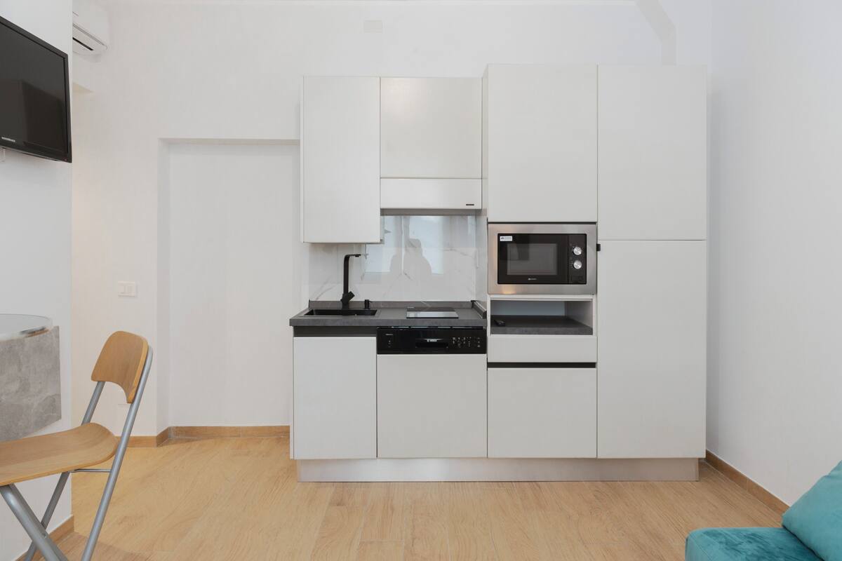 Una cocina compacta con armarios blancos, un microondas integrado y un lavavajillas.