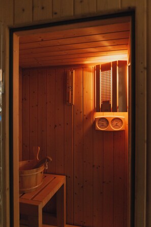 A wooden sauna room with a bench, a bucket, and two wall-mounted dials. - Residence I Tigli (Cinisello Balsamo)