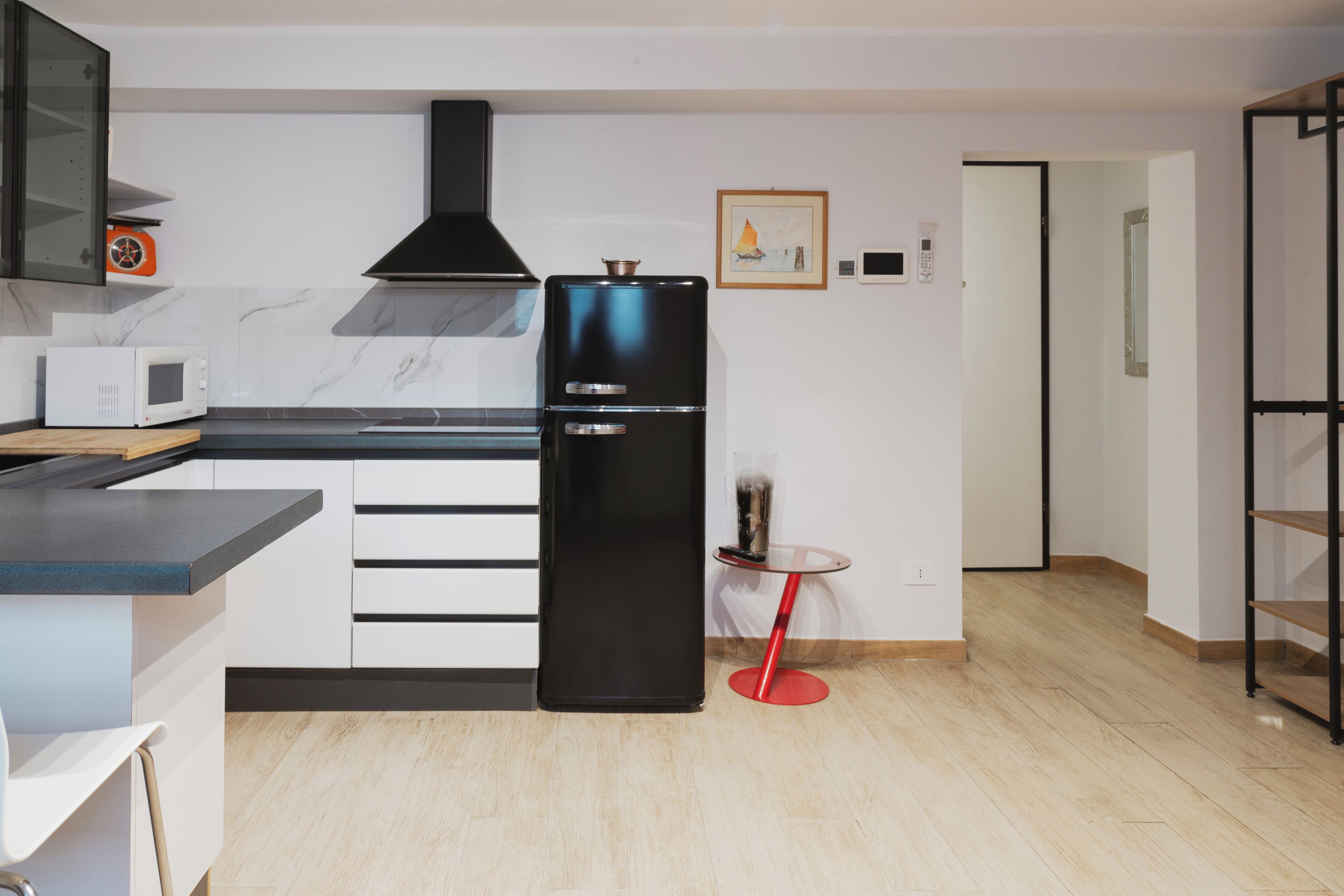 A modern kitchen with a black refrigerator, white cabinets, a microwave, and a small round table with a red base.