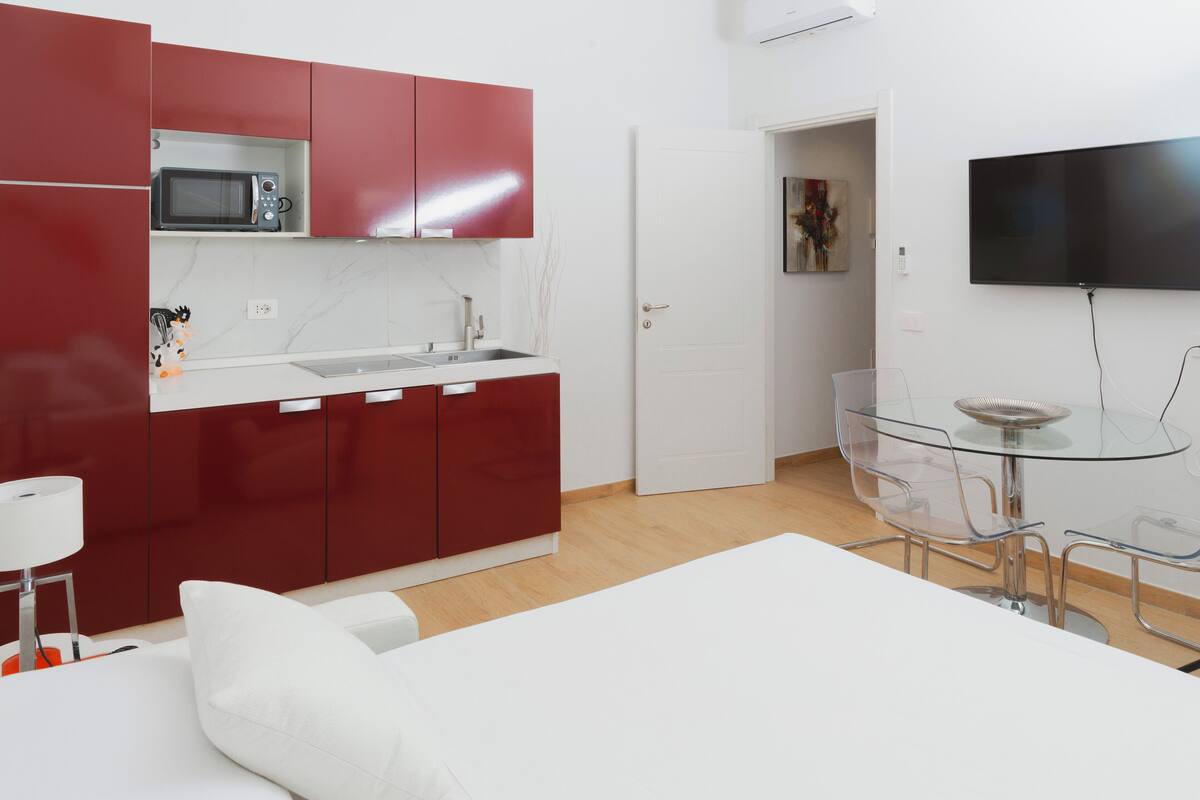 Una cocina moderna con armarios rojos, un microondas y una mesa de comedor de vidrio con sillas.
