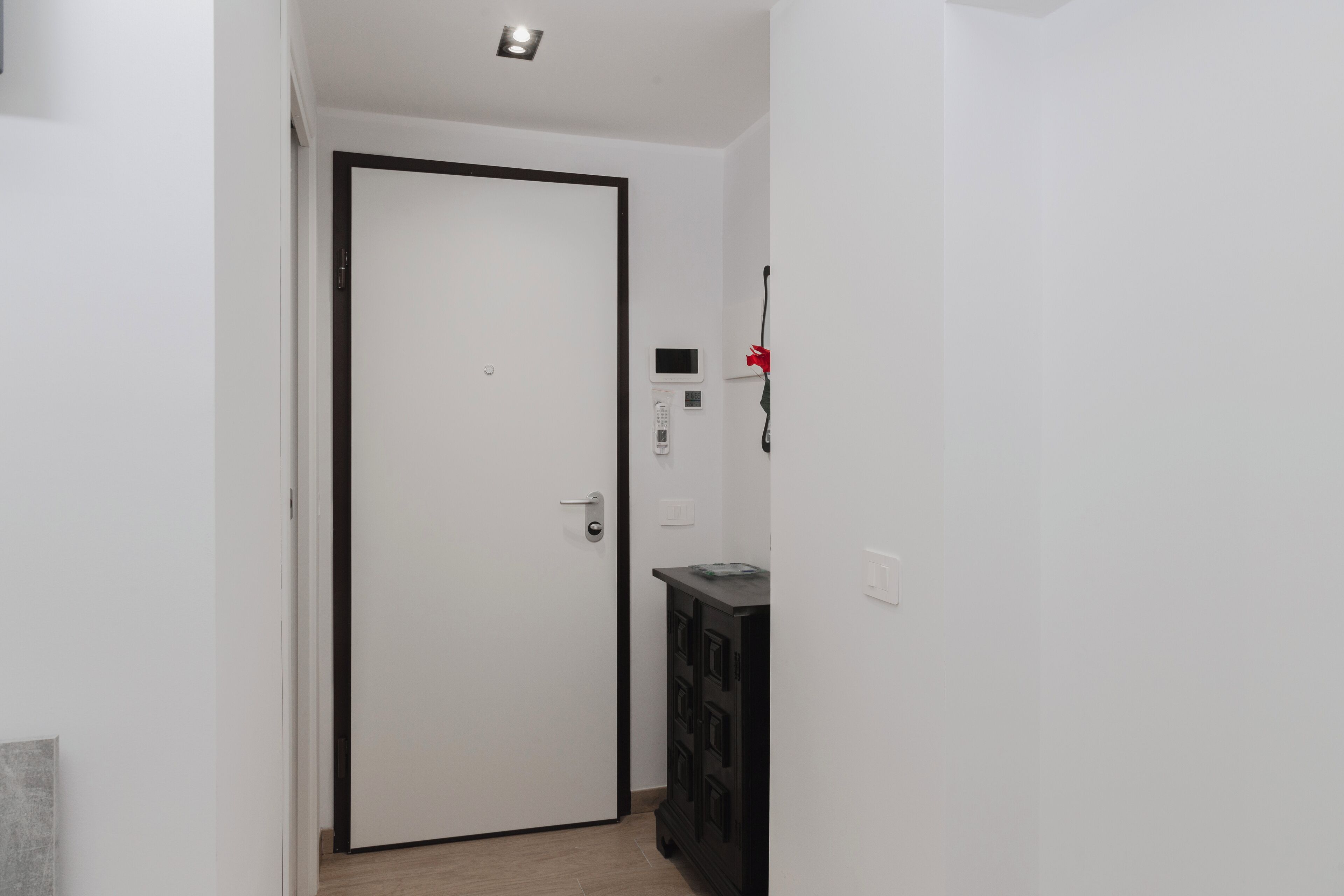 A hallway with a white door, a black cabinet, and a thermostat on the wall.