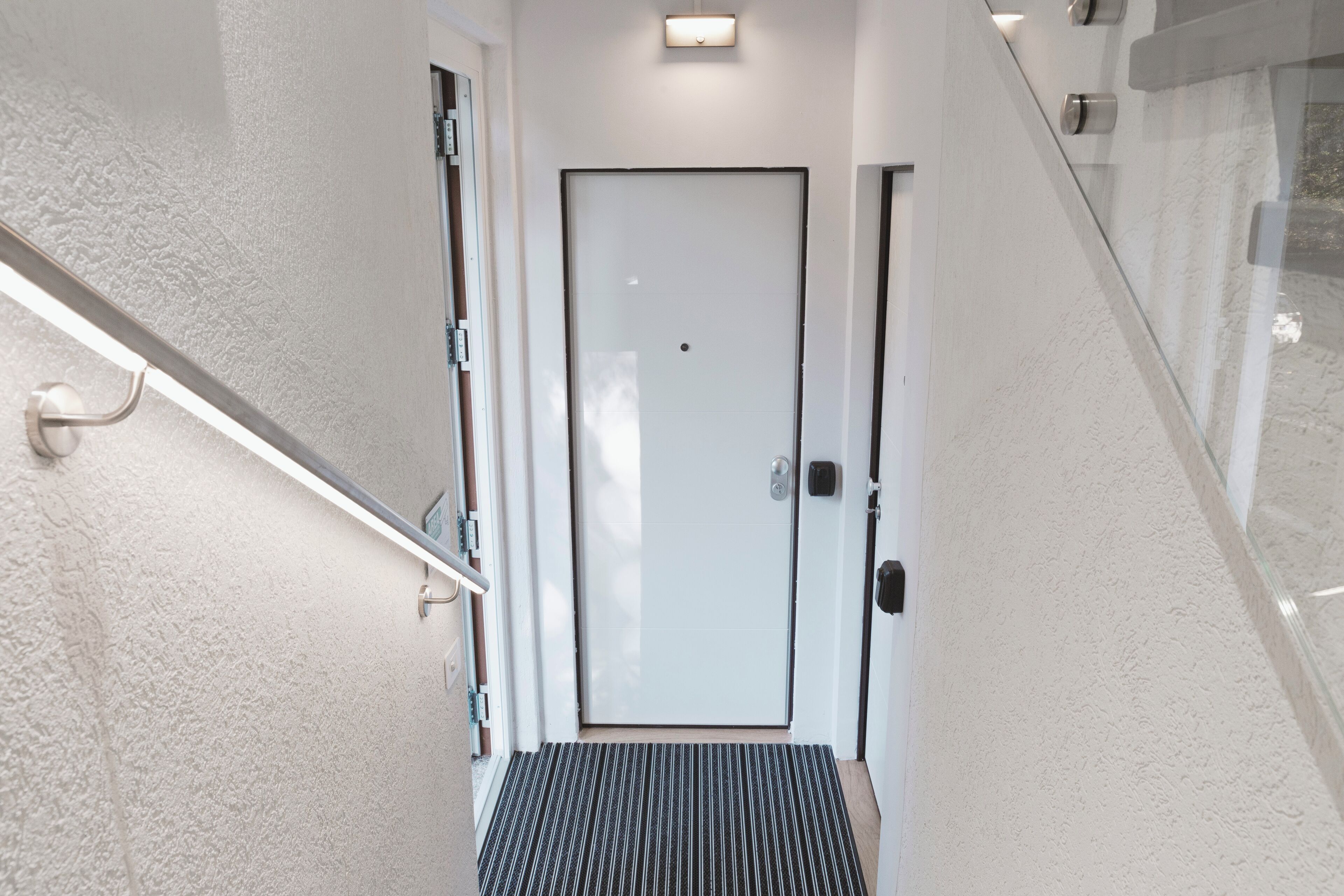 Una entrada de hotel moderna con puerta de cristal, barandilla metálica y pared con textura.