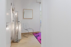 Una habitación con una silla transparente, una puerta blanca, un espejo y un tapete estampado.
