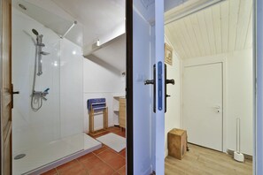 A bathroom with a glass shower enclosure, a wooden door, and a small wooden stool. - Casa Tib (Prunelli-di-Fiumorbo)