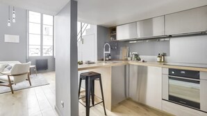 A modern kitchen with a large island, stainless steel appliances, and a view of the city through large windows. - Sun-filled Loft in the heart of the Marais (Paris)