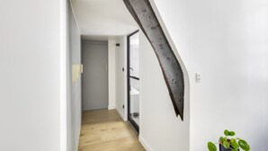 A narrow hallway with a wooden floor, a white wall, and a large, dark wooden beam protruding from the wall. - Sun-filled Loft in the heart of the Marais (Paris)