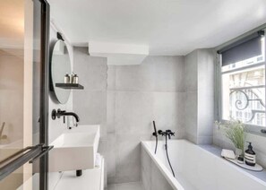 A modern bathroom with a white sink, a bathtub, and a window with a view of buildings.