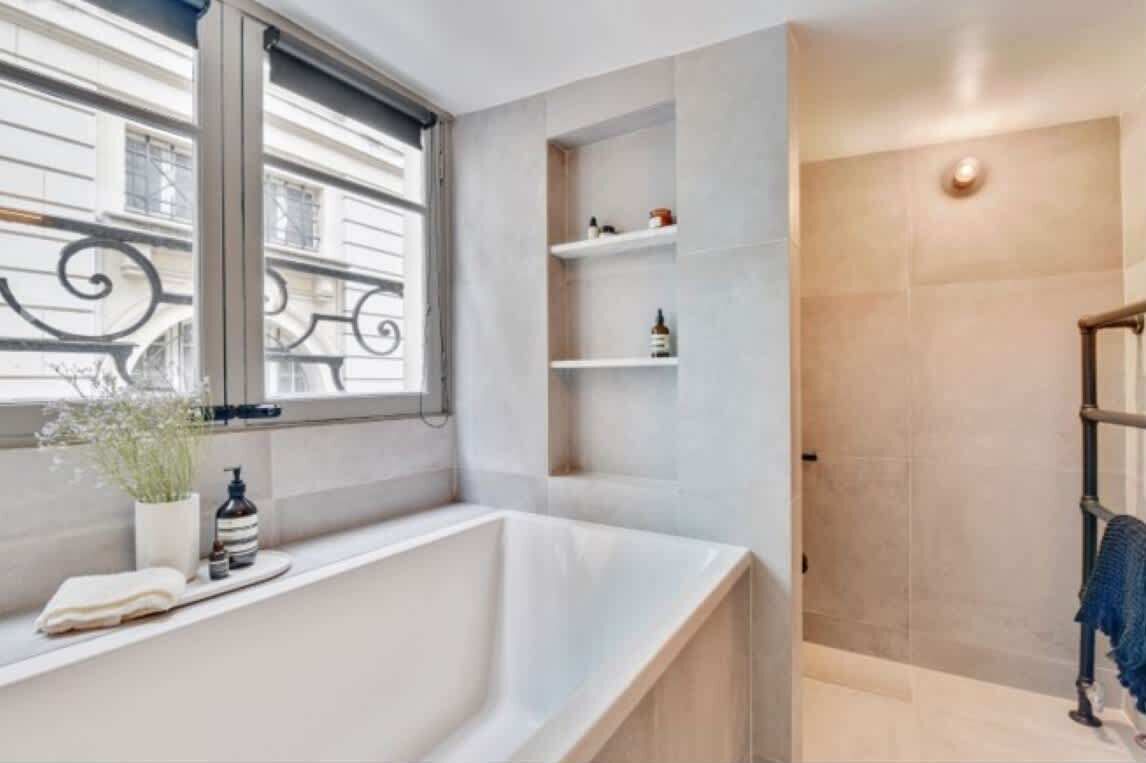 A modern bathroom with a freestanding bathtub, a window with decorative ironwork, and a shower area with a towel rack.
