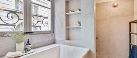 A modern bathroom with a freestanding bathtub, a window with decorative ironwork, and a shower area with a towel rack.