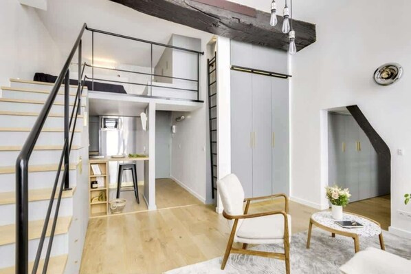 A modern loft-style apartment with a staircase leading to a lofted area, a dining table, and a seating area with a chair and a small round table.