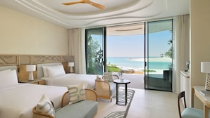 Een hotelkamer met twee bedden, een bank, rieten stoelen, een kleintje tafeltje en uitzicht op het strand.