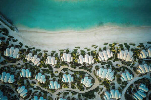 An aerial view of a resort with multiple overwater bungalows arranged in a curved layout along the shoreline, connected by pathways. - InterContinental The Red Sea Resort by IHG (Umluj)