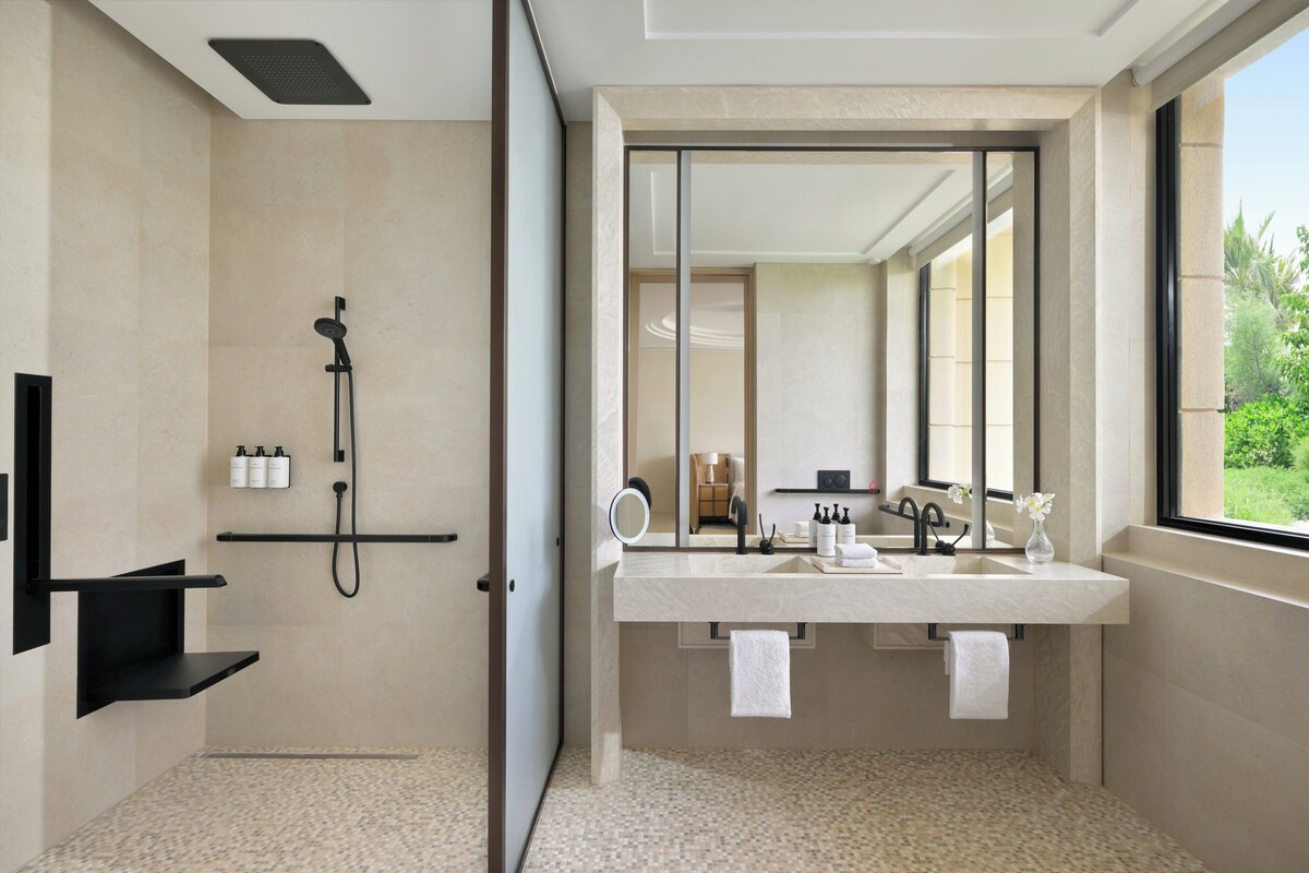 Une salle de bain moderne équipée d’une douche, d’un grand miroir, d’un meuble-lavabo et d’une fenêtre donnant sur l’extérieur.