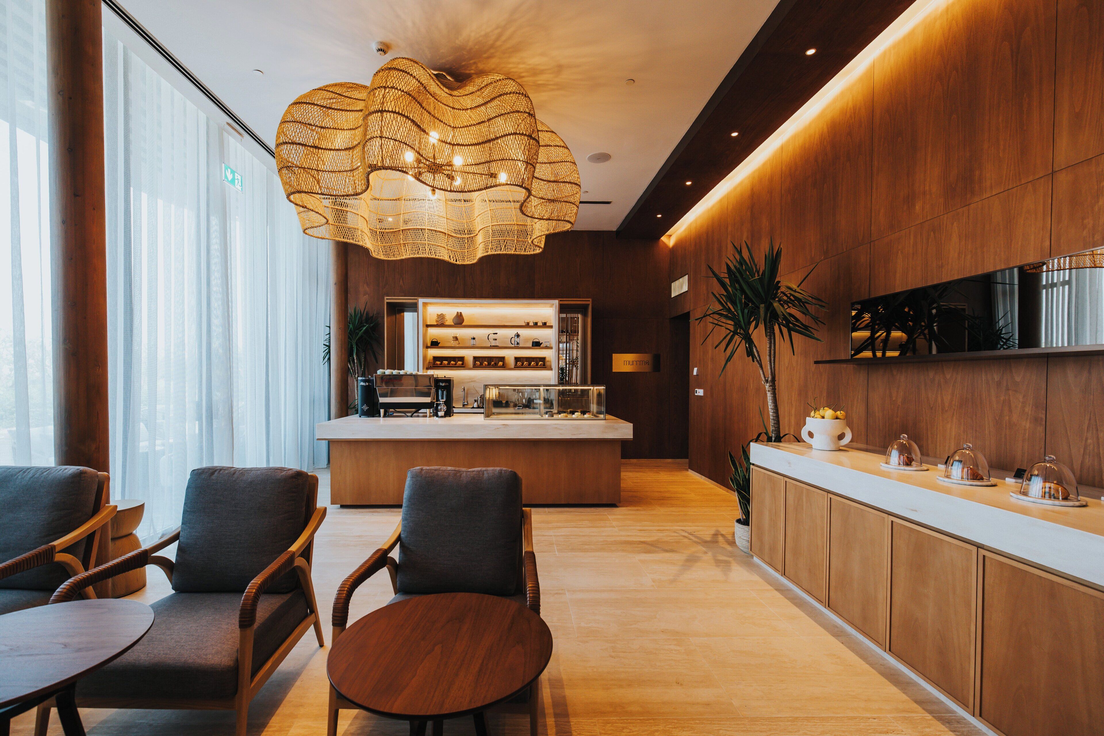 Un área de recepción moderna con un mostrador de madera, zona de estar con sillas y una gran lámpara decorativa.