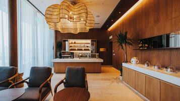 Un área de recepción moderna con un mostrador de madera, zona de estar con sillas y una gran lámpara decorativa.