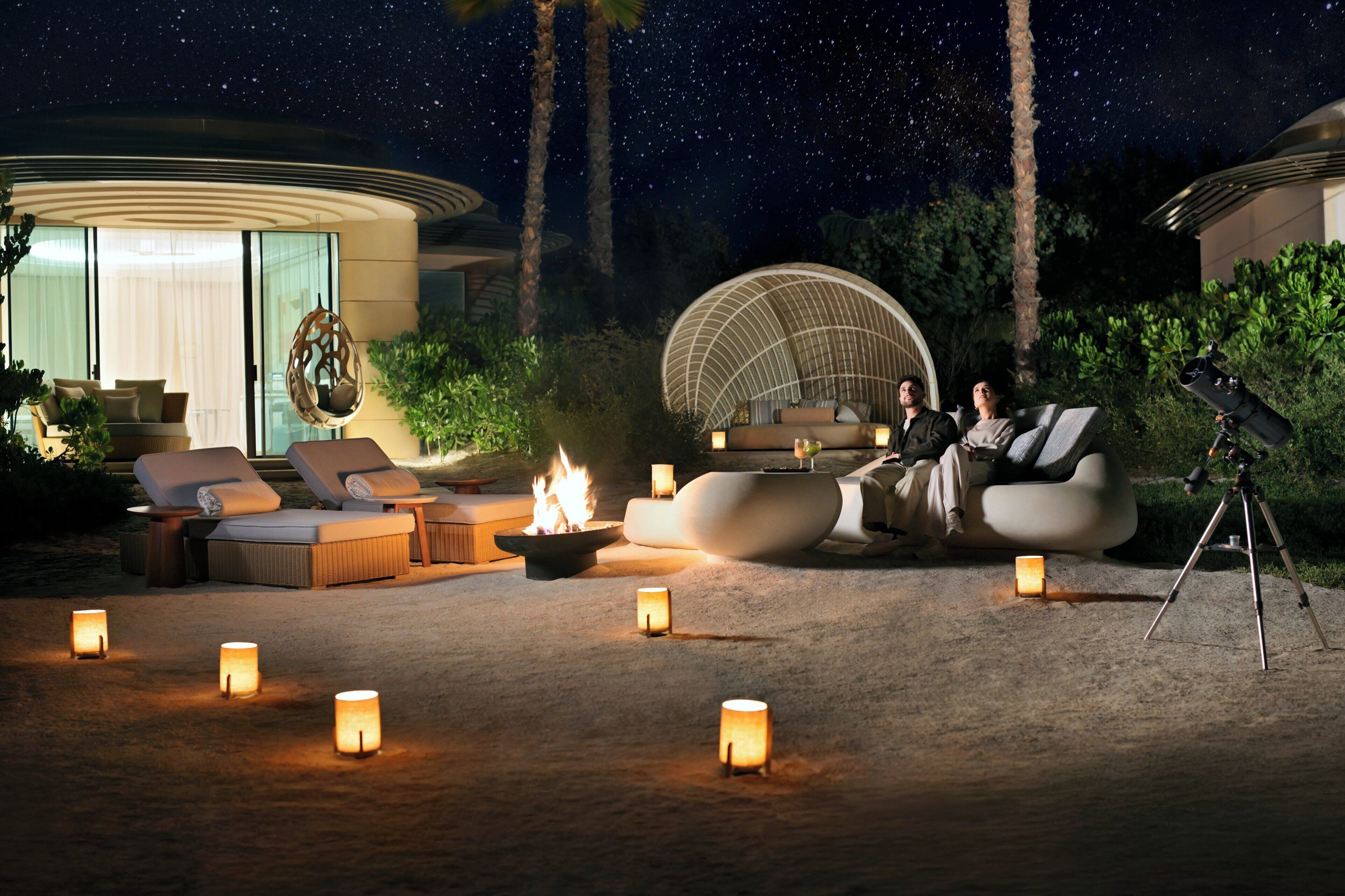 A night scene with outdoor seating, a fire pit, and a telescope.