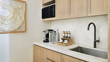 Cozinha com armários de madeira, pia de aço inoxidável, cafeteira, micro-ondas e um painel decorativo na parede.