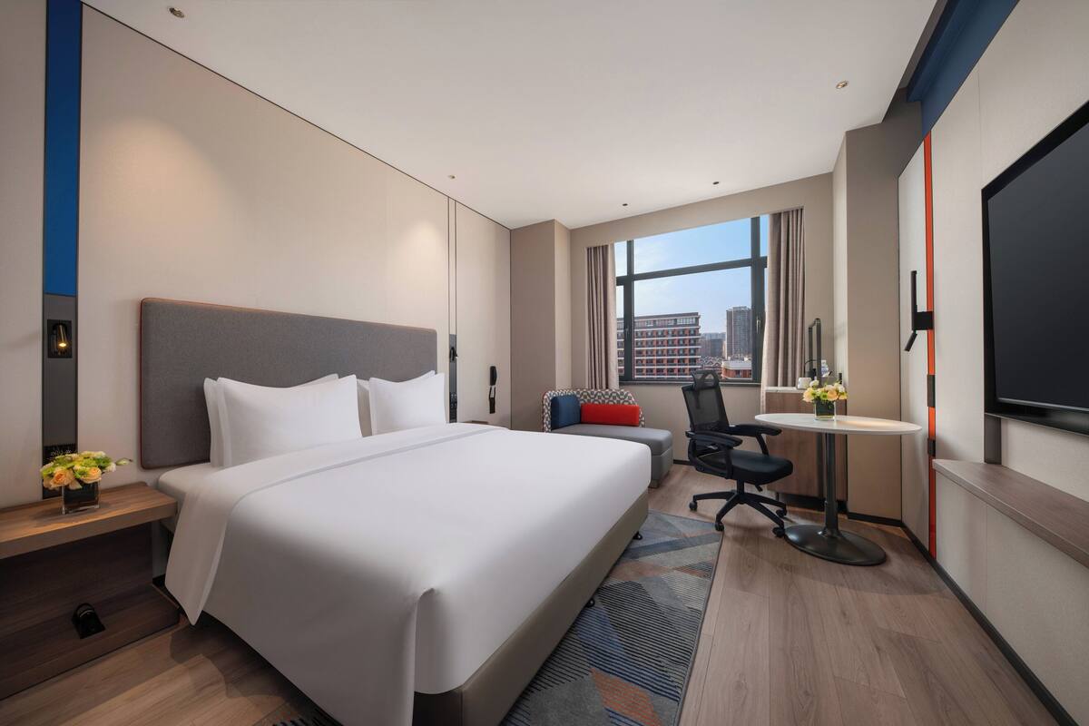Habitación de hotel moderna con una cama grande, un escritorio, una silla y un televisor.