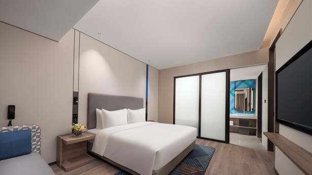 Una habitación de hotel moderna con una cama grande, un escritorio, un televisor de pantalla plana y una puerta corredera que da a un baño.