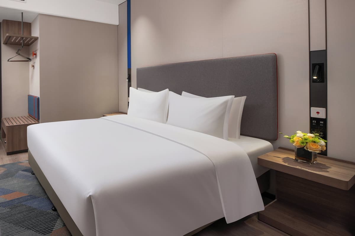 Una habitación de hotel moderna con una cama grande, una mesita de noche con un florero y un elevador de pared.