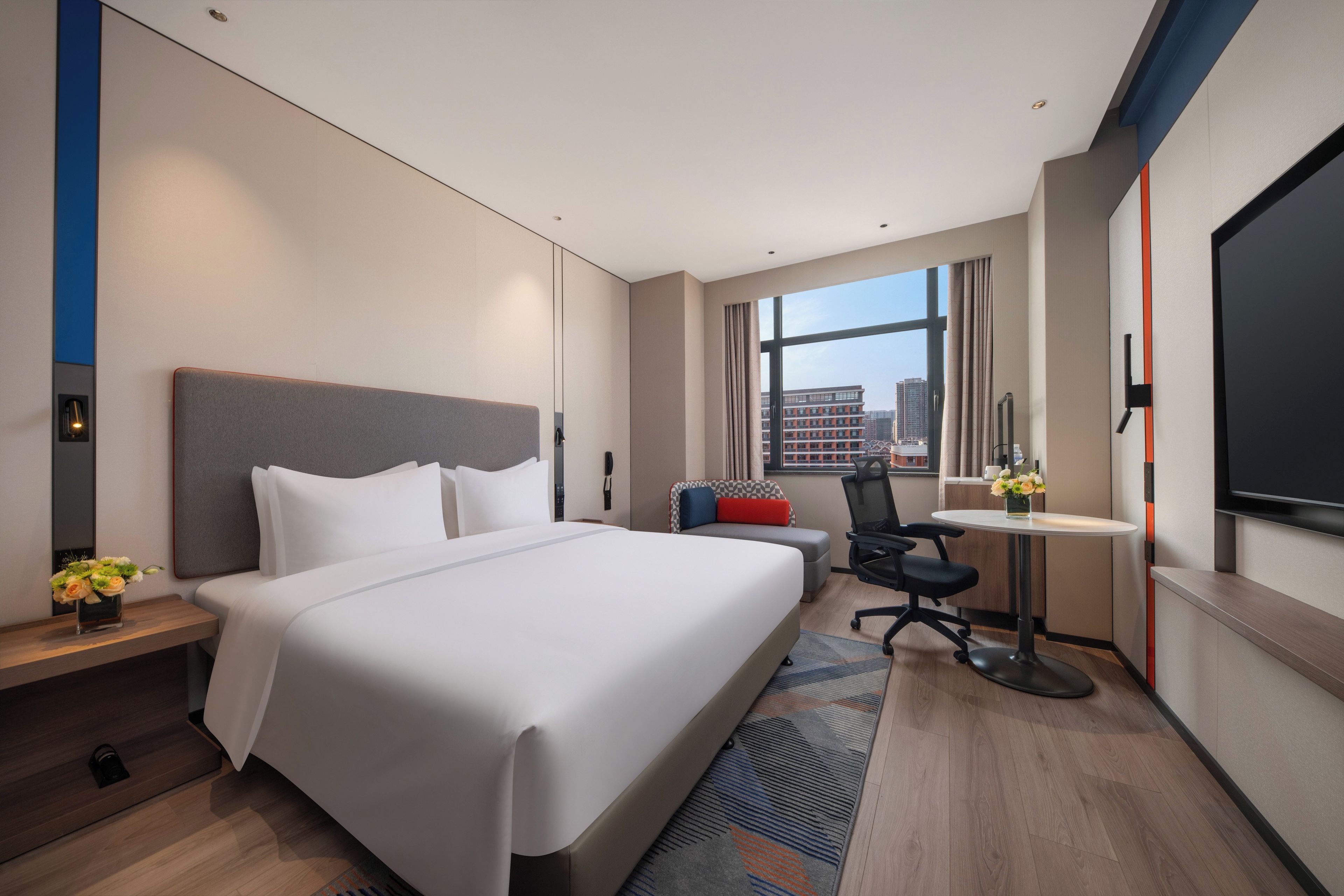 A modern hotel room with a large bed, a desk, a chair, and a TV.