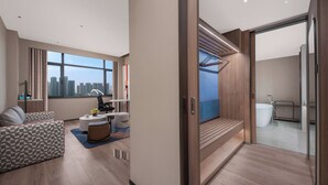 Habitación de hotel moderna con vista a la ciudad, una escalera de madera, un rincón de descanso con sofá y reposapiés, y un ventanal grande.