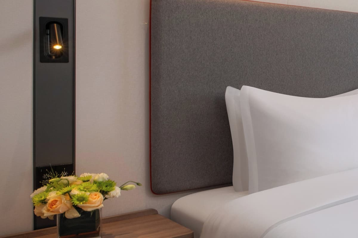 Habitación de hotel con una cama grande, una mesita de noche con un florero y una lámpara de pared.