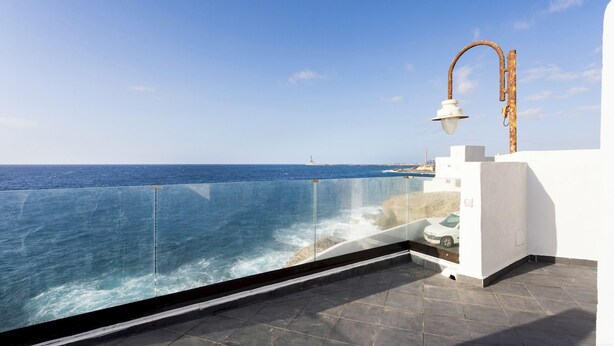 A balcony with a glass barrier overlooking the sea, a white wall, and a metal lamp post. - Home2Book Peaceful Apt & Sea View Terrace in Arico (Arico)