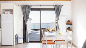 A modern kitchen with a white refrigerator, a dining table with orange cushions, and a view through a glass door. - Home2Book Peaceful Apt & Sea View Terrace in Arico (Arico)