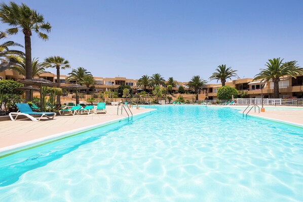 A swimming pool with lounge chairs and palm trees, surrounded by buildings.