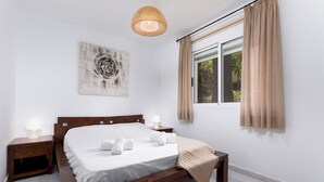 A bedroom with a wooden bed, white bedding, a bedside lamp, a wall-mounted artwork, and a window with curtains.