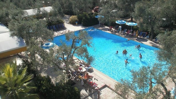 A swimming pool surrounded by trees, with people swimming and sunbathing. - Residence Baia Del Gallo (Vieste)