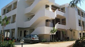 A modern multi-story building with a unique architectural design, featuring balconies and a car parked in front. - Residence Baia Del Gallo (Vieste)