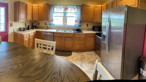 A kitchen with wooden cabinets, a stainless steel refrigerator, a dining table, and a window with floral curtains.