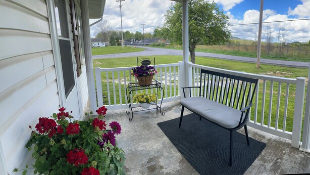 A porch with a bench, a welcome sign, and flower pots.