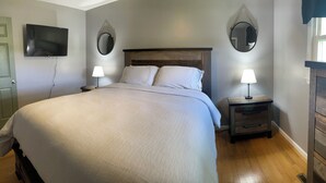 A bedroom with a bed, two bedside tables with lamps, a TV mounted on the wall, and a mirror.