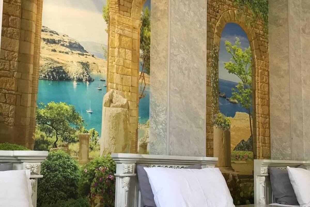 A hotel room with a mural of a coastal landscape, two beds, and a small table.