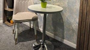 A chair and a small table with a potted plant in a room with a textured wall and a wooden shelf with plants. - Ammar hotel (Tashkent)