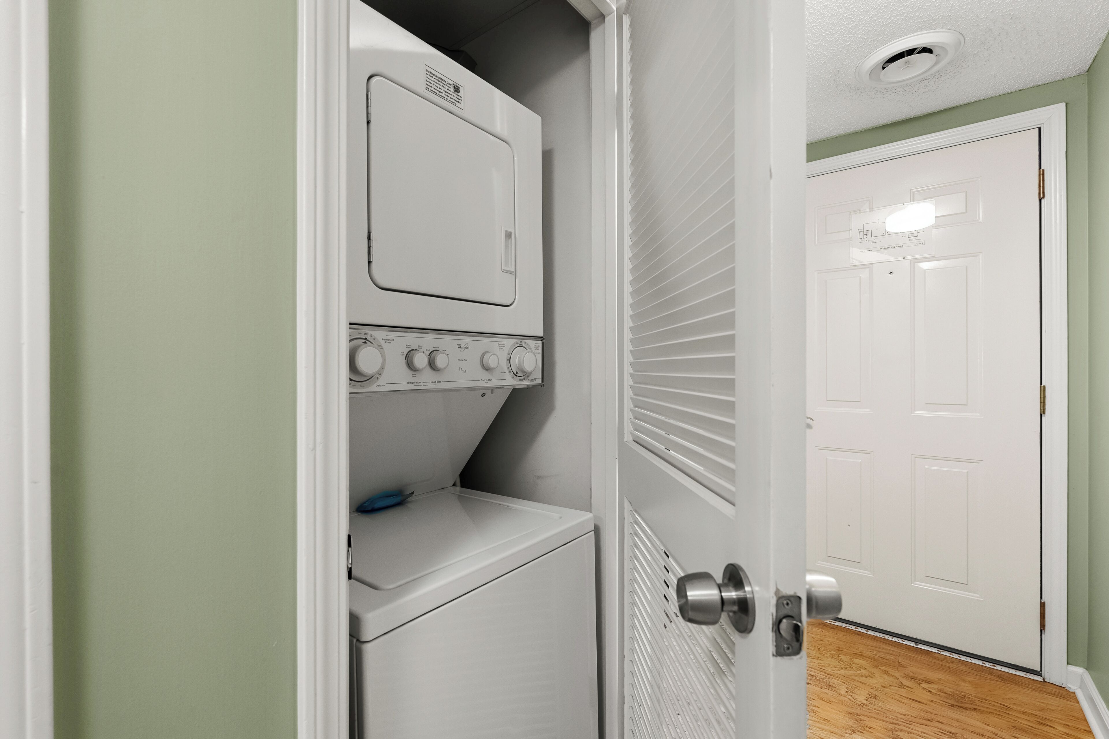 A laundry room with a washer and dryer, a door leading to another room, and a light switch on the wall.