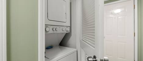 A laundry room with a washer and dryer, a door leading to another room, and a light switch on the wall.