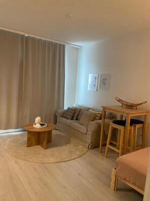 A modern living room with a sofa, a coffee table, a small wooden table with chairs, and a bed. - Charming 1-bedroom Apartment in Tampere With Fireplace (Tampere)