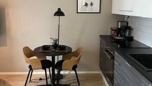 A modern kitchen with a dining area, featuring a round table with chairs, a clock, and a framed picture on the wall.