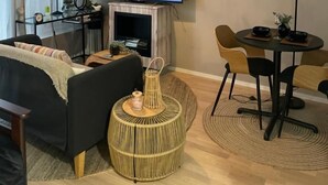 A modern living room with a flat-screen TV displaying the YouTube logo, a sofa, a coffee table, a dining table with chairs, a lamp, and a wicker side table.